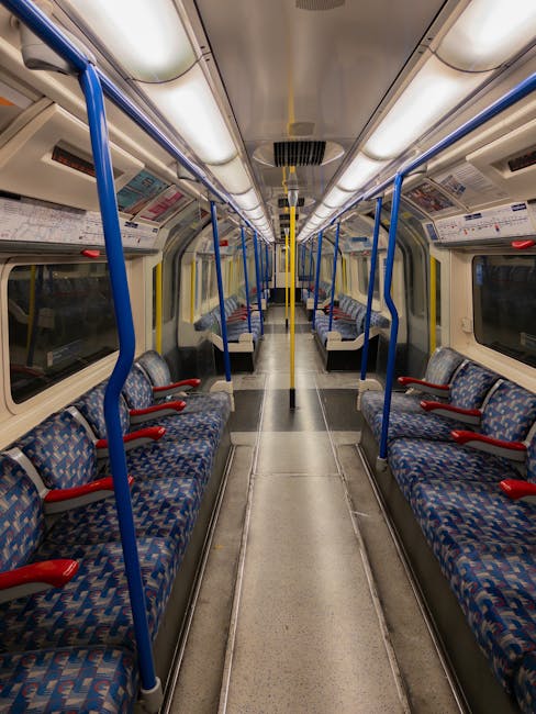 An empty interior of a modern metro train carriage with a clean, polished floor and neatly arranged black seating with colorful dotted upholstery on either side. Bright yellow handrails run along the 
